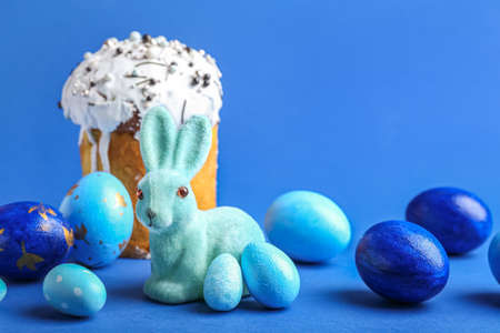 Cute Easter bunny, painted eggs and cake on blue background