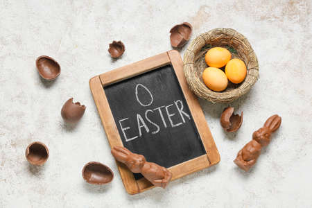 Chalkboard with word EASTER, chocolate bunnies and eggs on light background