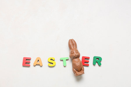Word EASTER made of colorful letters and chocolate bunny on light background