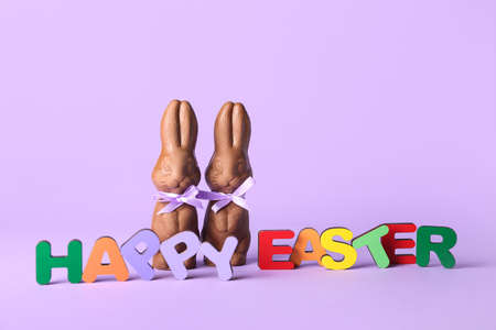 Text HAPPY EASTER made of colorful letters and chocolate bunnies on lilac backgroundの写真素材