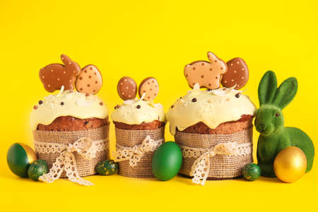 Delicious Easter cakes decorated with cookies and painted eggs on yellow background