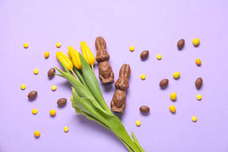 Composition with tulip flowers, chocolate Easter bunnies and candies on lilac backgroundの写真素材