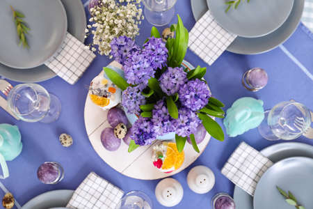 Vase with beautiful flowers, Easter cakes and eggs on served table