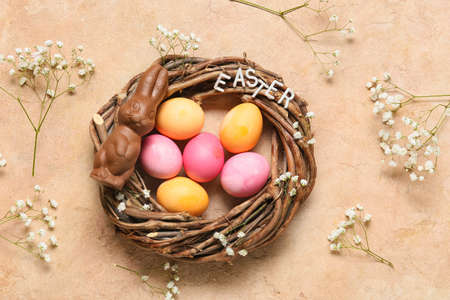 Nest with colorful Easter eggs, chocolate bunny and gypsophila flowers on color background