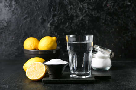 Glass of water, bowl with baking soda and ripe lemons on dark backgroundの写真素材