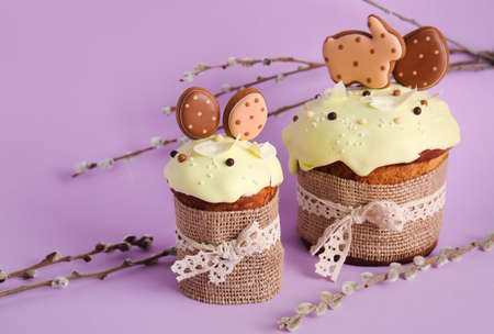 Delicious Easter cakes decorated with cookies and willow branches on purple background
