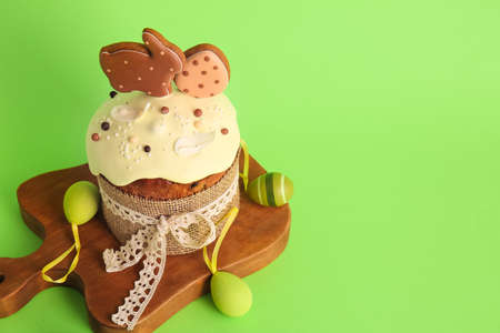 Board with delicious Easter cake decorated with cookies and painted eggs on green background
