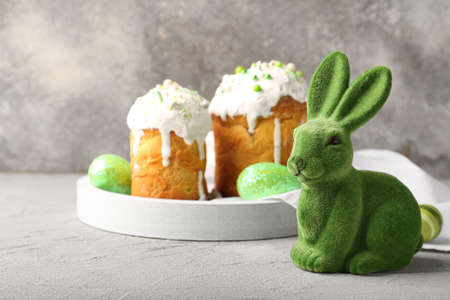 Cute Easter bunny with cakes and painted eggs on color background