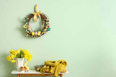 Table with beautiful tulips, knitted sweaters and Easter decor near color wall