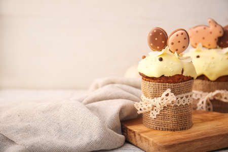Board with delicious Easter cakes decorated with cookies on light background