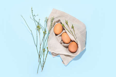 Easter eggs wrapped in napkin and herbs on color background