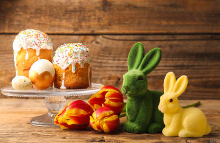 Cute Easter bunnies with cakes and flowers on wooden background