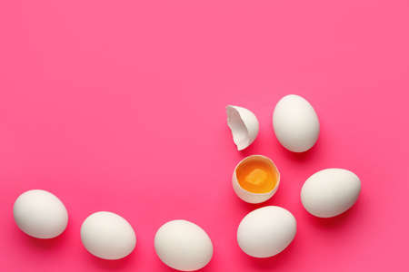 Cracked and whole chicken eggs on pink background