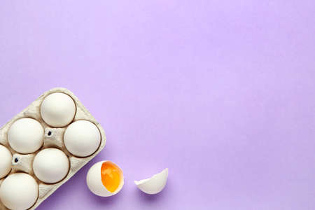 Cracked and whole chicken eggs in holder on purple backgroundの写真素材