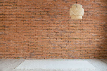 View of big empty room with brick wall, hanging lamp and carpet