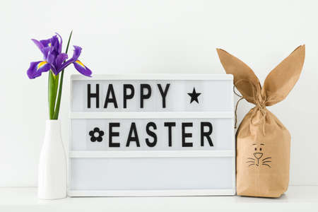 Paper bag bunny and board with text HAPPY EASTER on light background