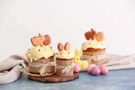 Wooden board with tasty Easter cakes decorated with cookies and eggs on color table