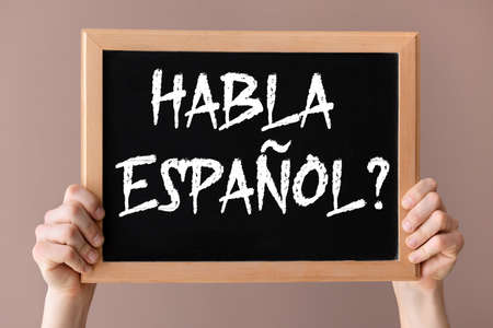 Hands holding chalkboard with text HABLA ESPANOL? (DO YOU SPEAK SPANISH?) on color backgroundの写真素材