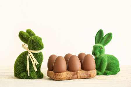 Holder with chocolate Easter eggs and green bunnies on light background