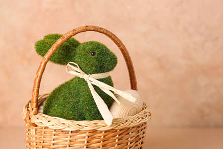 Wicker basket with green Easter bunny on color background, closeup