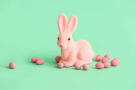Pink Easter bunny and candies on color background