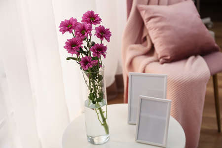 Vase with flowers and blank photo frames on tableの写真素材