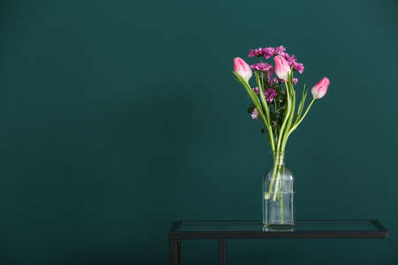 Vase with beautiful flowers on table near green wallの写真素材