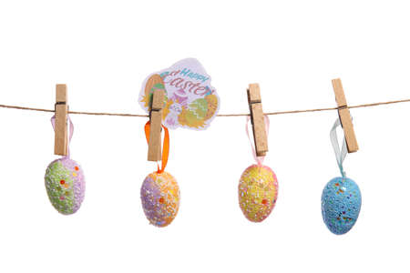 Easter eggs and greeting card hanging on rope against white background