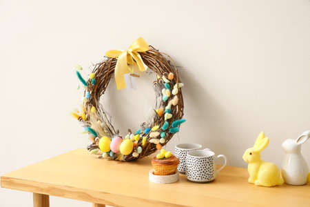 Delicious cake, cups and Easter decor on wooden bench near color wall