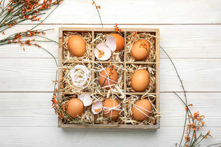 Box with Easter eggs and flowers on light wooden backgroundの写真素材