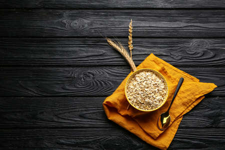 Bowl with raw oatmeal and spikelets on dark wooden backgroundの写真素材