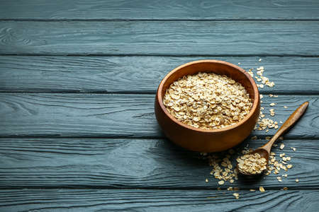 Bowl of raw oatmeal and spoon on dark wooden background