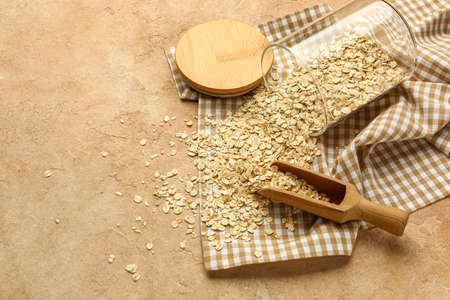 Overturned jar with raw oatmeal and scoop on color background