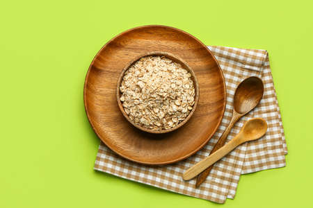 Bowl of raw oatmeal and spoons on green background