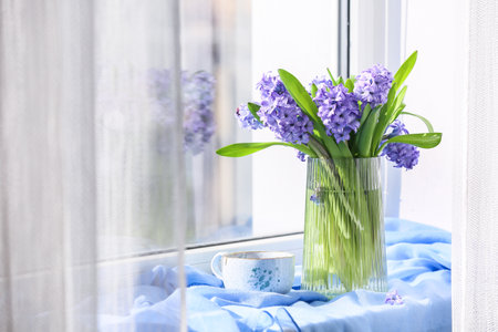 Vase with hyacinth flowers and cup of tea on windowsillの写真素材
