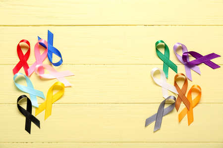 Colorful awareness ribbons on yellow wooden background. World Cancer Day