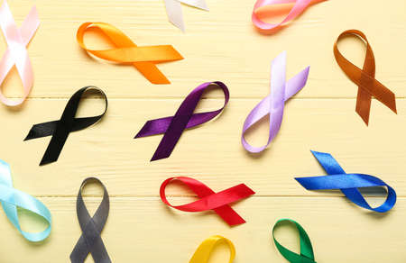 Set of awareness ribbons on yellow wooden background. World Cancer Day
