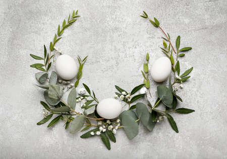 Stylish wreath with Easter eggs, eucalyptus leaves and flowers on light background