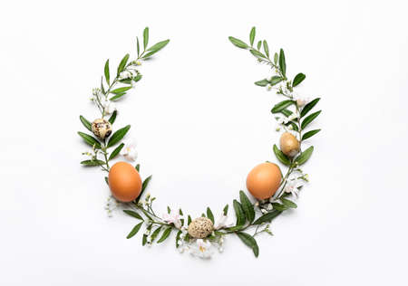 Stylish wreath with Easter eggs and flowers on light background