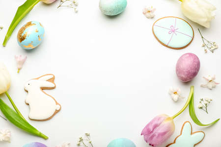 Stylish wreath with painted Easter eggs, cookies and flowers on white background