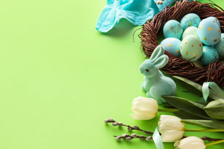 Nest with painted Easter eggs, tulip flowers and willow branches on green background