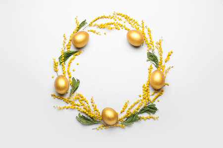 Stylish wreath with golden Easter eggs and mimosa flowers on light background