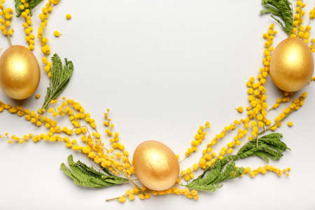 Stylish wreath with golden Easter eggs and mimosa flowers on light backgroundの写真素材