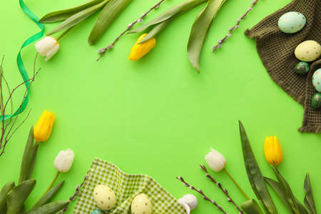 Frame made of painted Easter eggs, tulip flowers and willow branches on green backgroundの写真素材