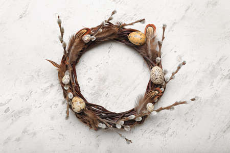 Stylish wreath with Easter eggs, feathers and willow branches on light backgroundの写真素材
