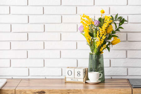 Beautiful flowers, cup of coffee and cube calendar with date 8 MARCH on kitchen counter. International Women's Day celebrationの写真素材
