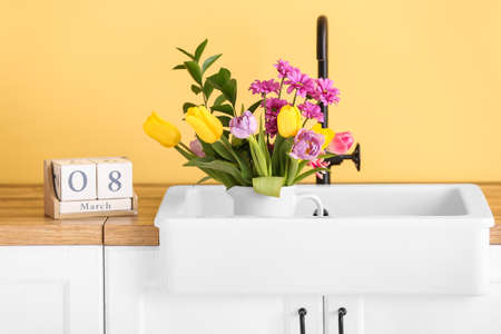 Bouquet of flowers in sink and cube calendar with date 8 MARCH on kitchen counter. International Women's Day celebrationの写真素材