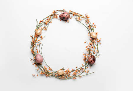 Stylish wreath with Easter eggs and flowers on light background