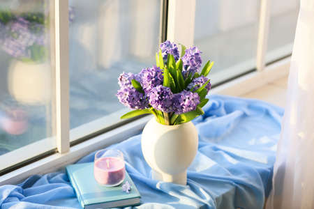 Vase with beautiful hyacinth flowers, candle and book on windowsillの写真素材