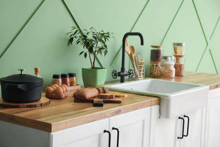 White sink with houseplant, food and kitchen utensils on counters near green wallの写真素材